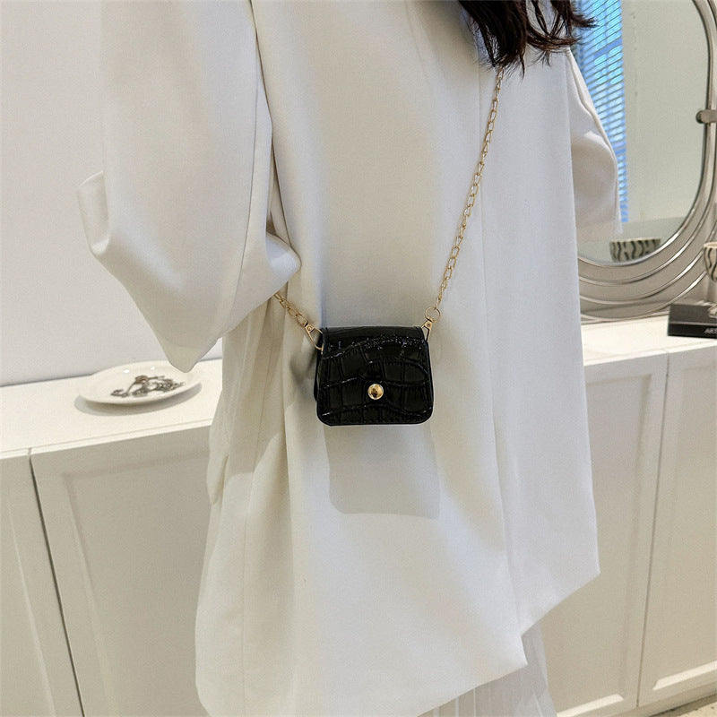 Person wearing a white outfit with a black handbag featuring a gold chain strap.